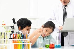 un niño y una niña asiáticos sonríen y se divierten mientras hacen experimentos científicos en el aula de laboratorio con el maestro. estudio con equipo científico y tubos. concepto de educación foto