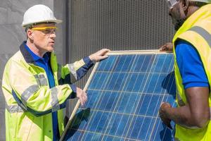 Selective focus at engineer face. African and Caucasian engineer inspect electrical solar panel at building construction site. Alternative energy and industrial concept. Outdoor shot. photo