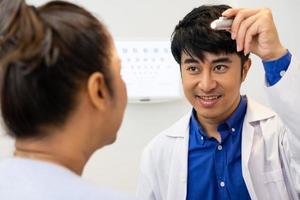 Selective focus at Optometrist face. While doctor using penlight and subjective refraction to  examine eye visual system of elder patient women with professional machine before made glasses. photo