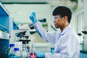 investigación de laboratorio de bioquímica, científico o médico en bata de laboratorio sosteniendo tubo de ensayo con reactivo con gota de líquido de color sobre equipo de vidrio que trabaja en el laboratorio. foto