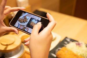 Selective focus at device screen. Women hand using smartphone to take photo of Japanese food for send or share with her friend or social network before eating. Human behavior, internet user.