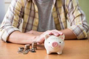 Selective focus at piggy bank. Men hand put hand to protect piggy bank full of coin on the table. Saving for retirement pension fund.  Close up indoor shot with casual cloth. photo