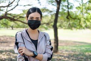 Selective focus at face of young beautiful Asian women wearing surgical face mask using smart watch to track activity before exercise or running at the park in the morning. New normal lifestyle. photo