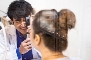 Selective focus at Optometrist face. While doctor using penlight and subjective refraction to  examine eye visual system of elder patient women with professional machine before made glasses. photo