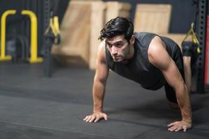 Handsome adult Caucasian men push up with trx robe to do crossfit exercise inside of fitness gym to workout for firm abs muscle and good body health. photo