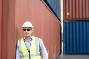 supervisor de carga de hombres caucásicos que usan chaleco y sombrero de seguridad mientras inspeccionan el estado de todos los contenedores, personas y trabajadores en la entrega, importación y exportación de carga. con espacio de copia foto