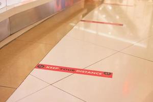 Selective focus at red sign on the floor in public area which promote and encourage people to keep distance from each other to prevent Covid or Coronavirus. New normal, Social distancing concept. photo