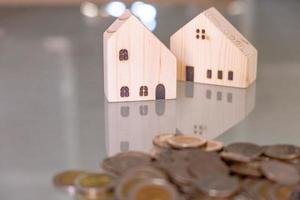 Selective focus at wooden house mock up that put on the top of growth money coins stack on the glass table with blurred background. Wealth and saving for home ownership and financial concept. photo