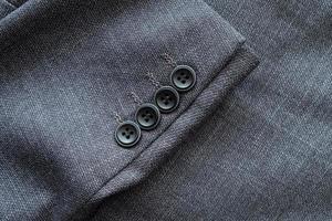 High resolution with details and quality shot of formal black or dark grey wool suit fabric texture. with button decoration under light and shadow ambient. Ideal for background or wallpaper. photo