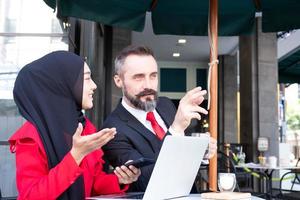 Smart business people with formal dress talking and meeting at outdoor coffee shop at business district area. And using laptop computer with smartphone. Diverse working environment with technology. photo