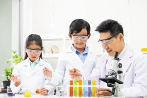 Young Asian boy and girl student wearing protective google while study and do science experiment in classroom with teacher. Learning and having fun moment. Chemist or biology classroom concept. photo