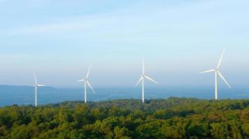 paisaje puesta de sol toma de granja de turbinas eólicas en el campo de hierba verde con cielo azul claro y montaña en el fondo. energía verde alternativa que genera electricidad a partir de la energía eólica natural. foto