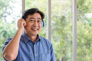 Portrait shot of Senior elder Asian man wearing wireless headphone device listening to music, feeling happy with smile on face. Healthy hearing condition with old person concept with copy space. photo