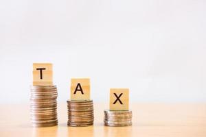 Selective focus at wood tax sign on top of decrease stack of money on the white copy space background. Business or personal tax payment, expense that need to manage and plan. photo