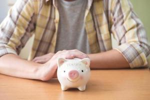 Selective focus at piggy bank. Men hand put hand to protect piggy bank full of coin on the table. Saving for retirement pension fund.  Close up indoor shot with casual cloth. photo