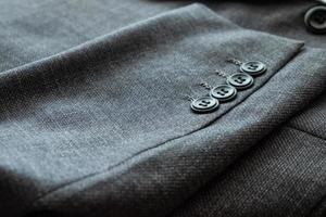 Blurred defocus shot of formal black or dark grey wool suit fabric texture. with button decoration under light and shadow ambient. Ideal for background or wallpaper. photo