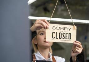 Young women business owner with apron walking to the front glass door of the shop to hang close sign at the entrance before closing the store. photo