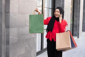 Beautiful East Asian Islamic women wearing hijab. Smile and feeling happy and holding many shopping bags walking in urban city area or department store. People lifestyle concept.