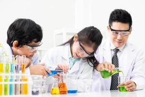 Young Asian kids wearing white scientist gown and do chemical test tube while study, learning in science classroom with teacher. Young children education concept by experiment, fun and enjoy classroom photo