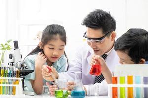 Selective focus at face. Young Asian boy and girl smile and having fun while doing science experiment in laboratory classroom with Teacher. Study with scientific equipment and tubes. Education concept photo