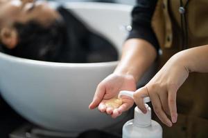 la mano de la peluquera presiona la botella de champú o acondicionador antes de usarla para lavar al cliente dentro del estudio de peluquería. concepto de producto y servicio de belleza y moda. foto