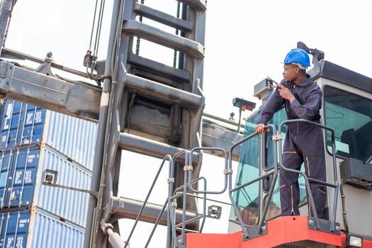 Selective focus at face of Black African logistic worker wearing safety equipment, check and inspection while loading container while talking and communicate with his team by  radio device. photo