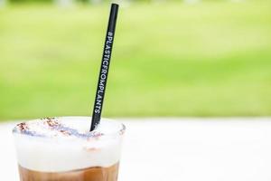 Selective focus at Cold coffee drink with Composable plastic straw with Green grass natural blurred background. Environment conservation, Travel and Holiday concept. photo