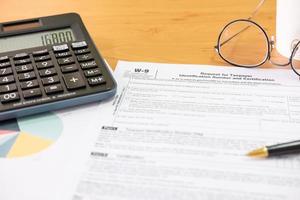 Selective focus Calculator button. American US tax form on wooden table. With blurred calculator, pen and glasses. Taxation time obligation for people who has income that need to comply to regulation. photo