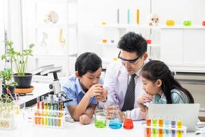 un niño y una niña asiáticos sonríen y se divierten mientras hacen experimentos científicos en el aula de laboratorio con el maestro. estudio con equipo científico y tubos. concepto de educación