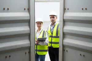 supervisor de carga de hombres y mujeres caucásicos que usan chaleco y sombrero de seguridad mientras inspeccionan el estado de todos los contenedores, personas y trabajadores en la entrega, importación y exportación de carga. foto