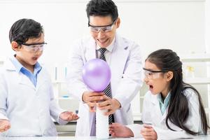 Selective focus on girl face. Young Asian boy and girl smile and having fun while doing science experiment in laboratory classroom with Teacher. Study with scientific equipment and tubes.
