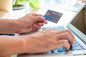 enfoque selectivo en la maqueta de la tarjeta de crédito. los hombres sostienen la tarjeta de crédito y escriben información de seguridad en el teclado de la computadora para realizar transacciones de pago en línea. actividad financiera segura en línea. foto