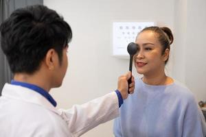 Selective focus at Optometrist face. While doctor using penlight and subjective refraction to  examine eye visual system of elder patient women with professional machine before made glasses. photo