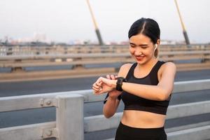 enfoque selectivo en la cara de las jóvenes y hermosas mujeres asiáticas que usan un reloj inteligente para rastrear la actividad y escuchar música mientras se calientan antes de hacer ejercicio o correr en la vista urbana de la ciudad. estilo de vida saludable y en forma. foto