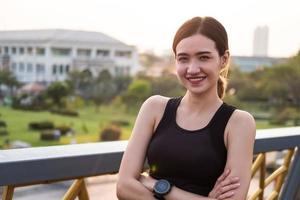 Selective focus at face of young beautiful Asian women using smart watch to track activity and listen music while warm up before exercise or running at the urban city view. Fit and healthy lifestyle. photo