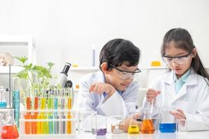 Young Asian boy and girl smile and having fun while doing science experiment in laboratory classroom with Teacher. Study with scientific equipment and tubes. Education concept. photo