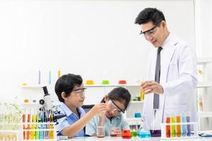 Young Asian boy and girl student wearing protective google while study and do science experiment in classroom with teacher. Learning and having fun moment. Chemist or biology classroom concept. photo