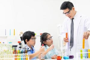 Young boy and girl doing science experiment with colorful liquid chemical inside glass tube and beaker. With teacher who teach and give instruction in classroom. Science and education concept. photo