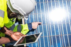 Selective focus at digital tablet. African and Caucasian engineer inspect electrical solar panel and record information into mobile tablet. Alternative energy and industrial concept. Outdoor shot. photo