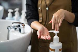 la mano de la peluquera presiona la botella de champú o acondicionador antes de usarla para lavar al cliente dentro del estudio de peluquería. concepto de producto y servicio de belleza y moda. foto