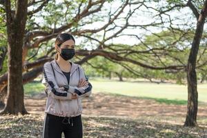 Selective focus at face of young beautiful Asian women wearing surgical face mask using smart watch to track activity before exercise or running at the park in the morning. New normal lifestyle. photo