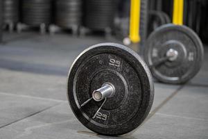 enfoque selectivo en la placa de peso de hierro unida a la barra en el piso dentro del gimnasio con fondo borroso de la máquina de levantamiento de pesas para la construcción muscular con espacio de copia. concepto de objeto deportivo foto