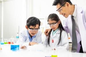 Young Asian boy and girl student wearing protective google while study and do science experiment in classroom with teacher. Learning and having fun moment. Chemist or biology classroom concept. photo