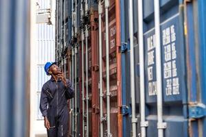 Selective focus at face of Black African logistic worker wearing safety equipment, check and inspection the condition of container while talking and communicate with his team by  radio device. photo