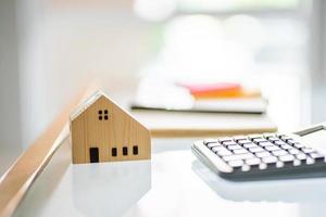 Selective focus at house mock up. With blurred calculator and  on wooden desk. Personal financial saving concept for home loan, mortgage investment, tax or house ownership concept. photo