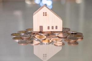 Selective focus at wooden house mock up that put on the top of growth money coins stack on the glass table with blurred background. Wealth and saving for home ownership and financial concept. photo