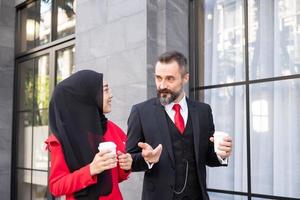 Selective focus at women face. Outdoor shot of Smart Business man and women in formal suit holding coffee cup while standing at Central Business district in the. Diverse people working environment. photo