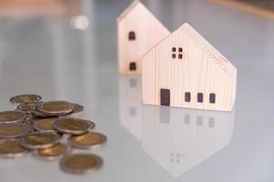 Selective focus at wooden house mock up that put on the top of growth money coins stack on the glass table with blurred background. Wealth and saving for home ownership and financial concept. photo