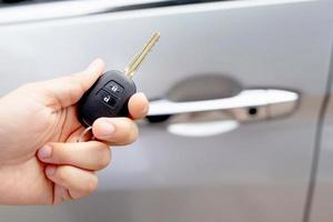 A man holding a car key in front of a car at a showroom photo