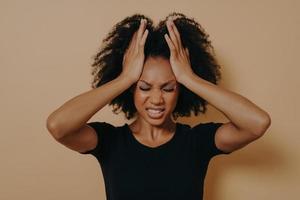 Shocked panic African American girl dressed in black T-shirt holding hands on head photo